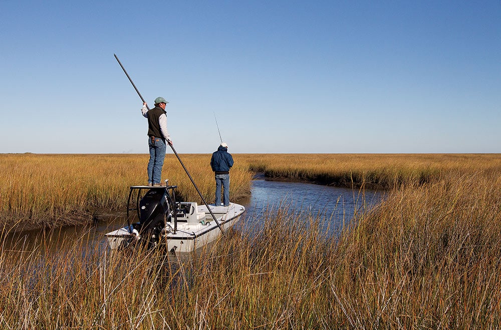 Anglers poling fishing boat skiff for bull redfish in Louisiana channel